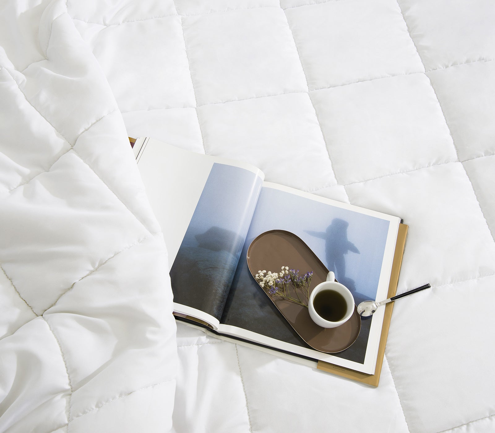 Entspannungs-Moodbild: Weiche Ganzjahresbettdecke aus Mikrofaser mit Buch, Kaffee und Blüten – perfekter Schlafkomfort